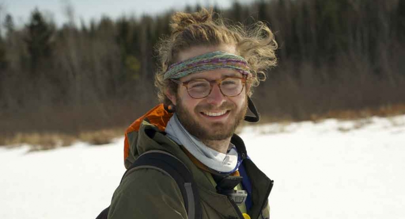 a gap year student smiles at the camera while standing in a field of snow. there are trees in the background.